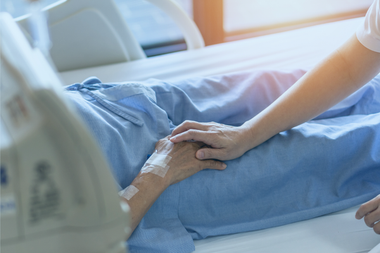 A healthcare worker holding a patient's hand in a hospital bed.